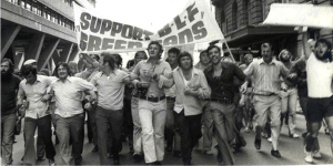 Black and white photograph of a group of men marching with arms interlinked. Banner reads 'Support BLF Green Bans'.