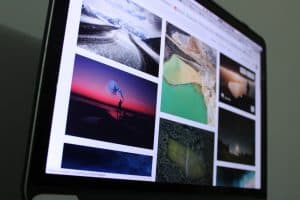 A computer screen displaying colourful, striking images, like a result of a google search. Most are out of focus, but in focus is a grand glacial valley, and a human figure silhouetted against the sunset, holding a bright flare.