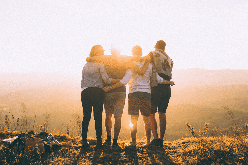 A group of friends stand with arms around each other looking out across a valley.