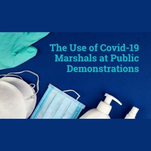text reads The use of Covid-19 marshals at public demontrations. Framing the text are a rubber glove, masks and hand sanitisers