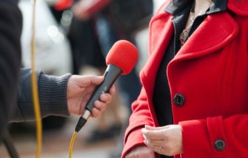 a person holding a red microphone is interveiwing a person wearing a red jacket. You can see their upper torsos but not their heads.