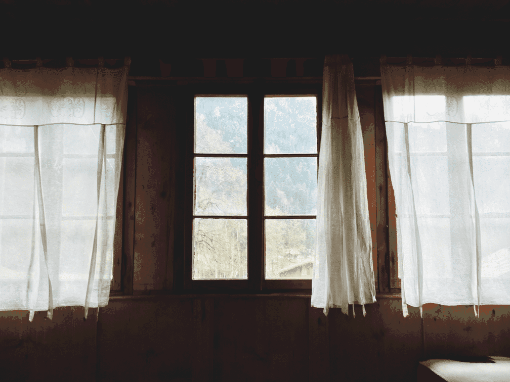 Photograph of a window with curtains opening.