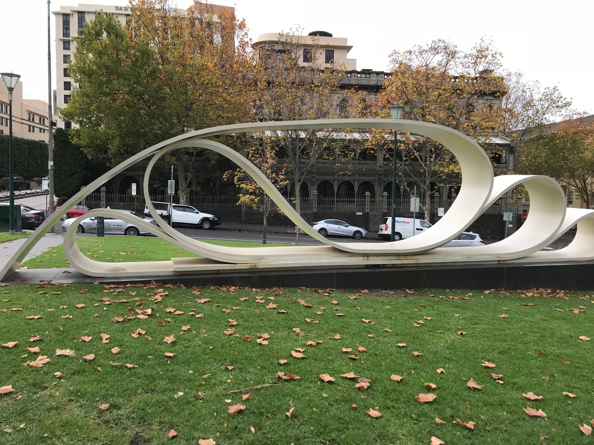 Photo of a sculpture in a park. The sculpture is made of metal and replicates a large piece of paper folded over making loops.