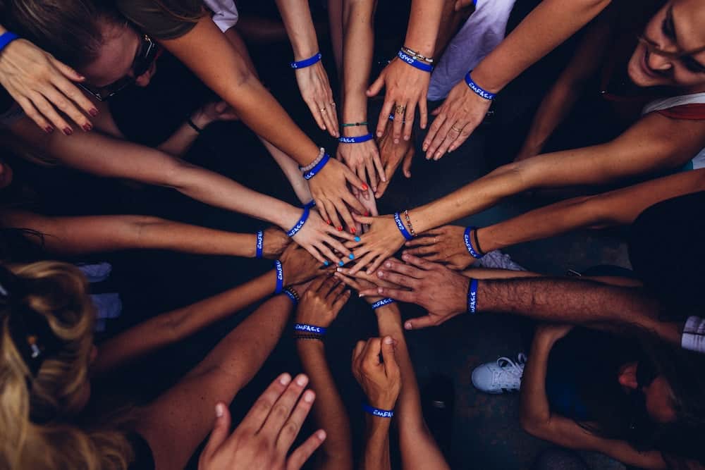 Over a dozen hands reach into the middle of a circle, making the 'all in' symbol