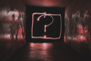 Photograph of a neon question mark in a dark room.
