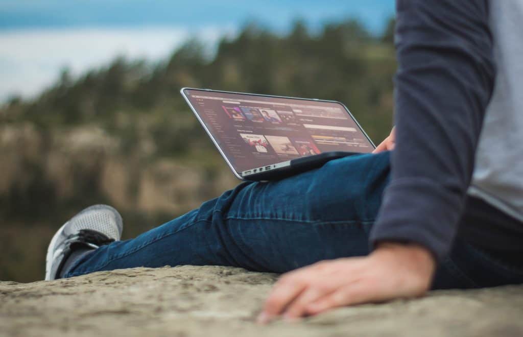 A person sitting outside on a rock, with a laptop on their lap