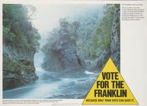 Yellow triangle with words that read - vote for the franklin. The triangle is on top of an image of Rock Island Bend, a rock formation in the Franklin River. Steep rock cliffs with forest frame the river flowing towards a large rock outcrop that the river flows around.